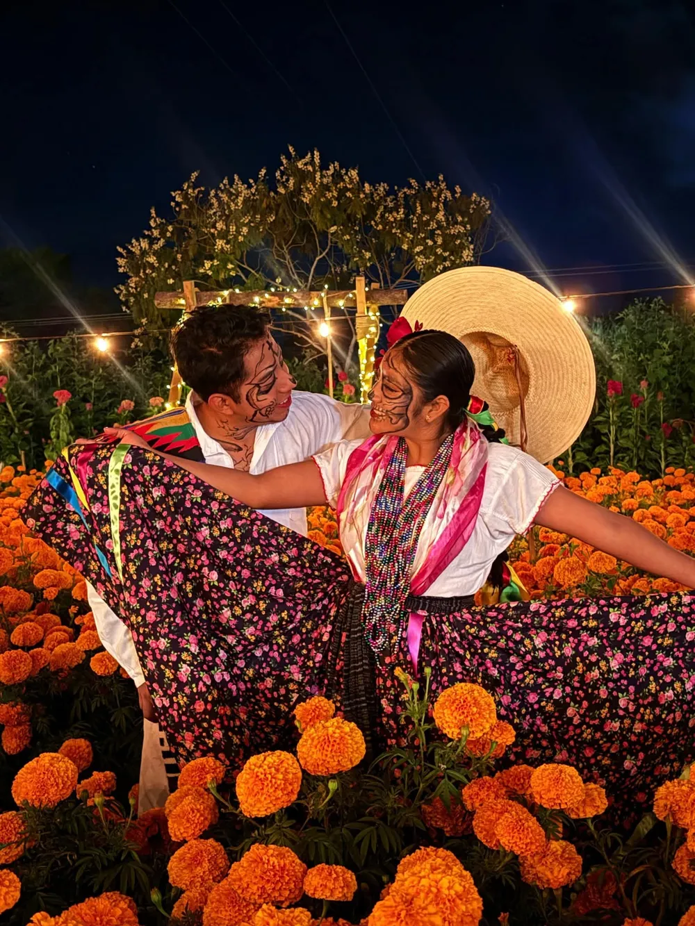 Pareja del grupo Raíces de Jalieza bailando con traje típico y maquillaje de catrina entre flores de cempasúchil